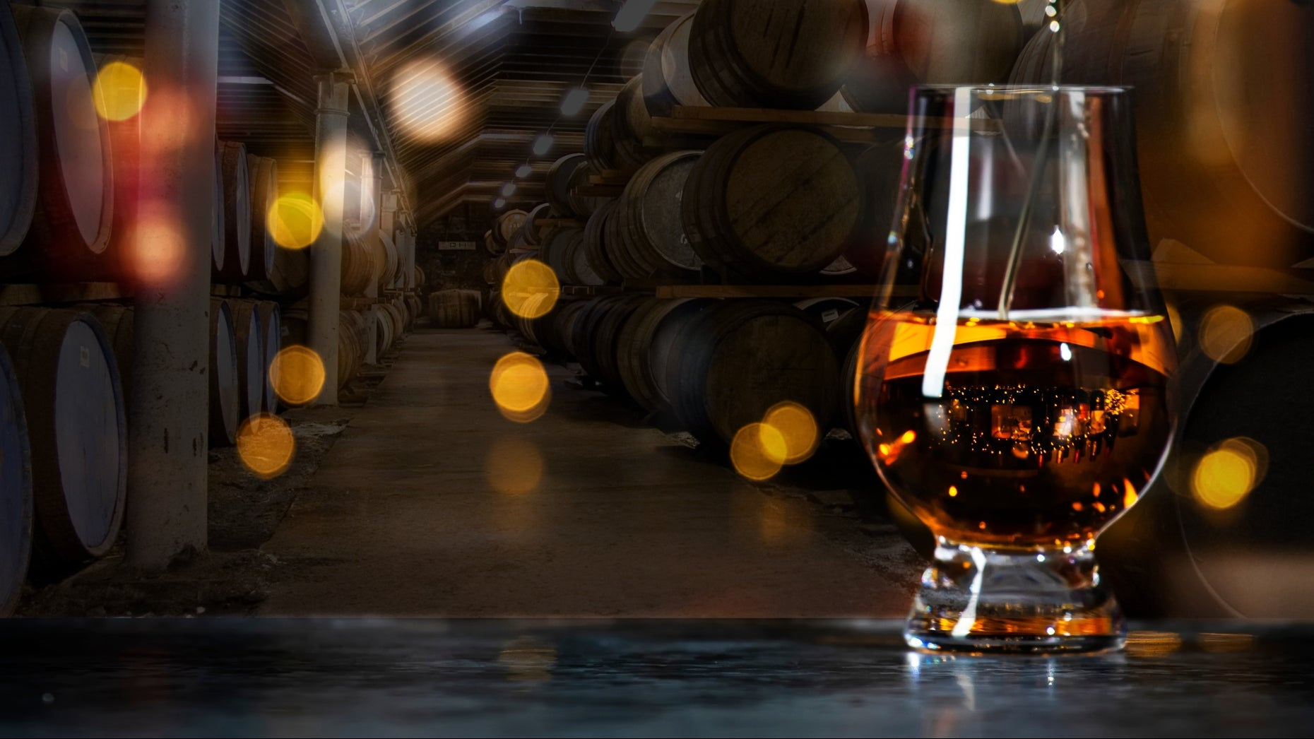 Glass of whiskey in front of whiskey barrels with warm lighting